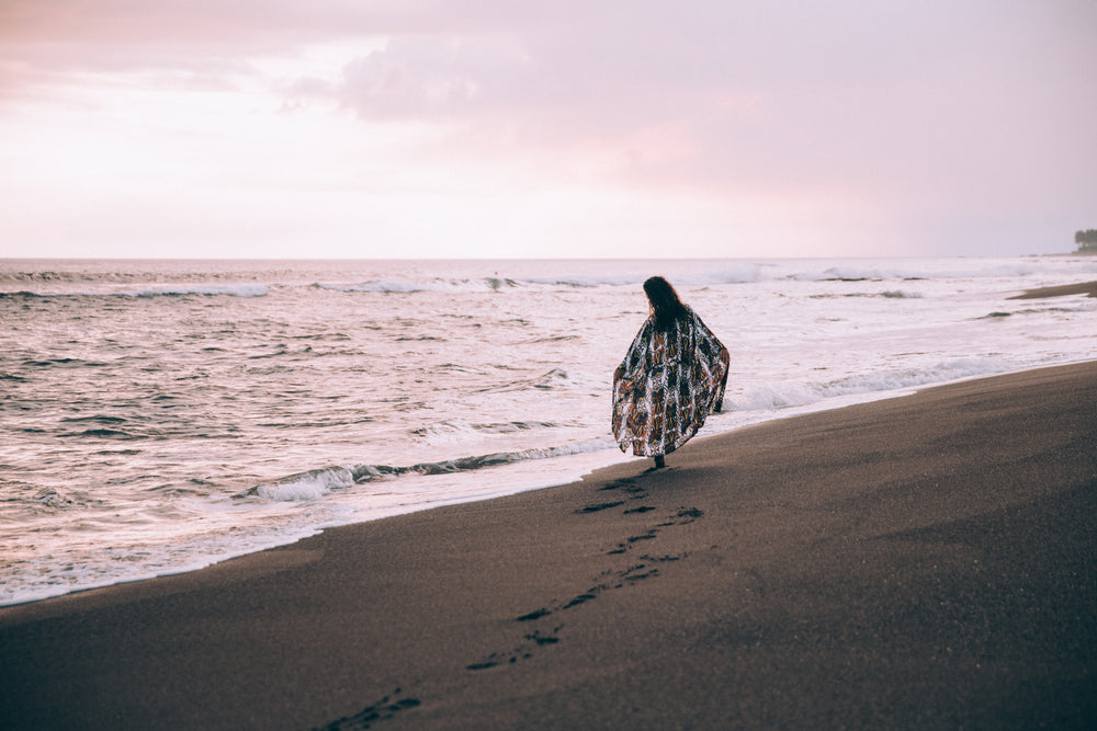 a woman walks along the beach leaving footprints in the sand