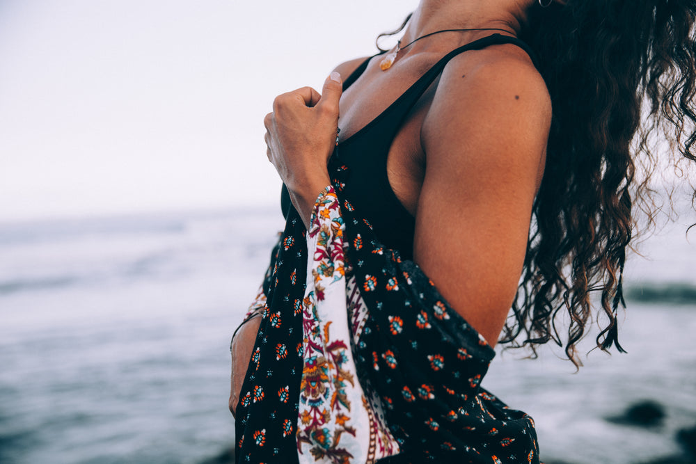 a woman with patterned robe throws head back by beach