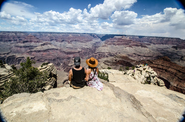 a young woman and man sit overlooking a canyon