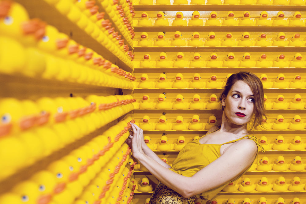 a young woman leans by a wall of ducks and looks away