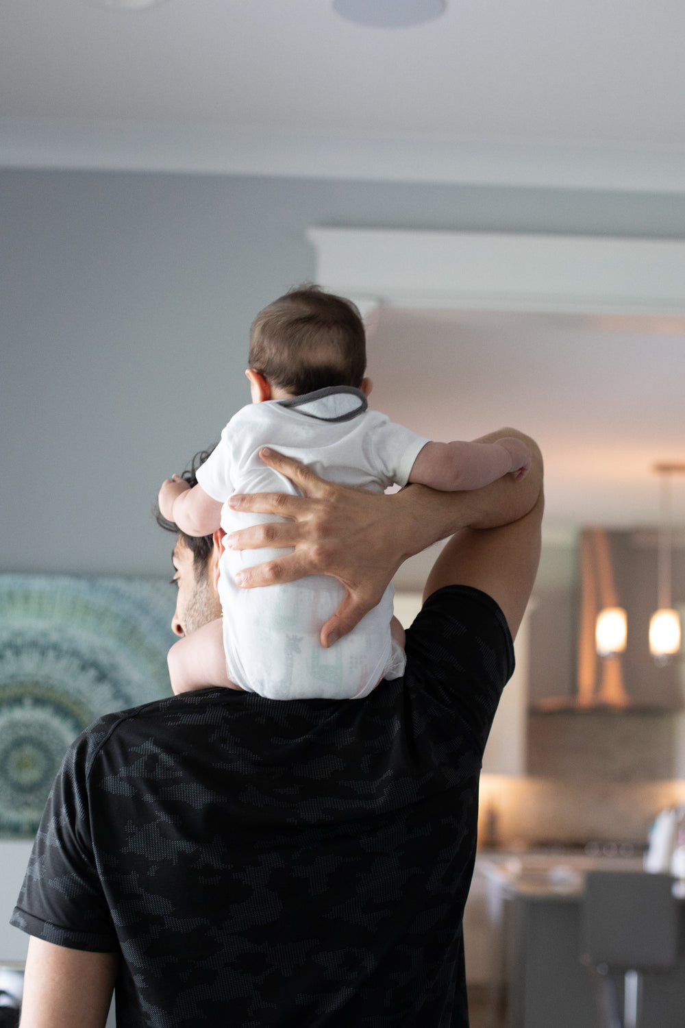 adult faces the wall and holds a baby on shoulders
