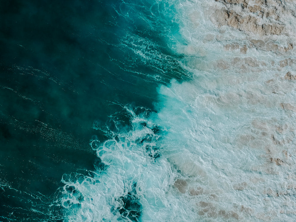 aerial photo of waves hitting the sandy shore