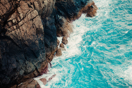 aerial view of aqua blue waves and a rocky cliff