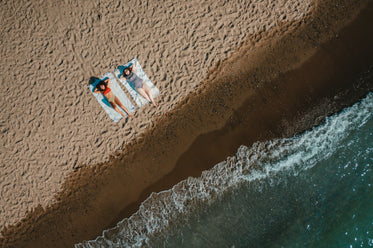 aerial view of sandy beach with two women laying on blankets