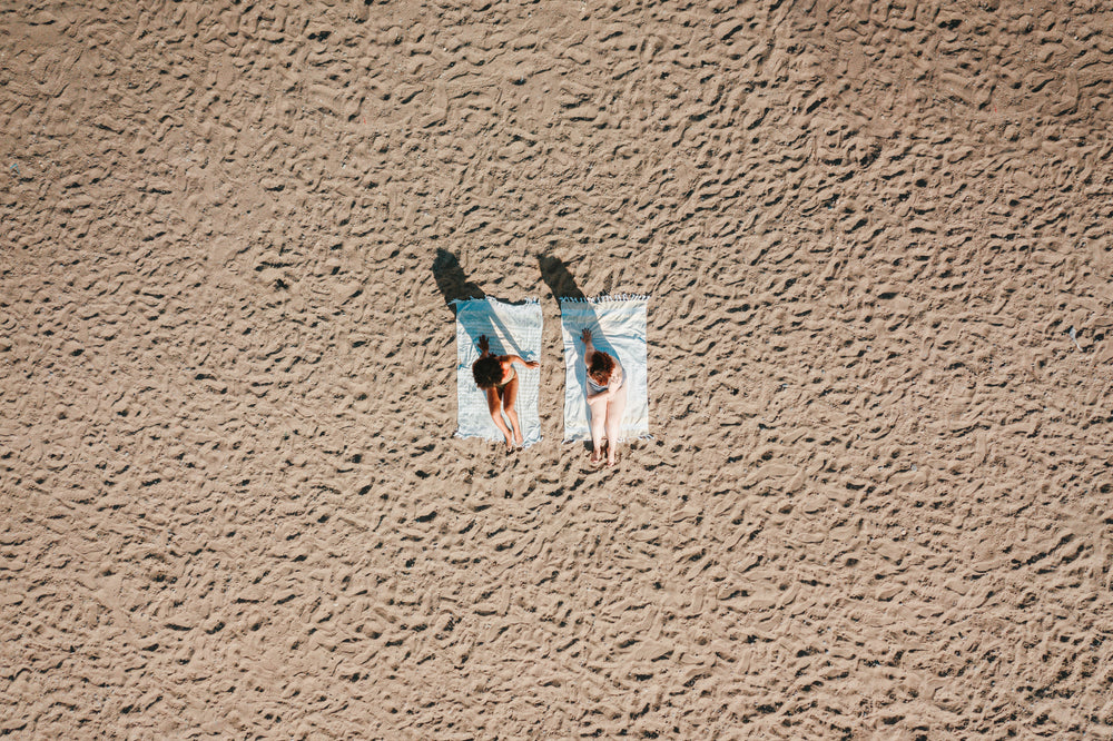aerial view of two women sitting on sandy beach in sunshine