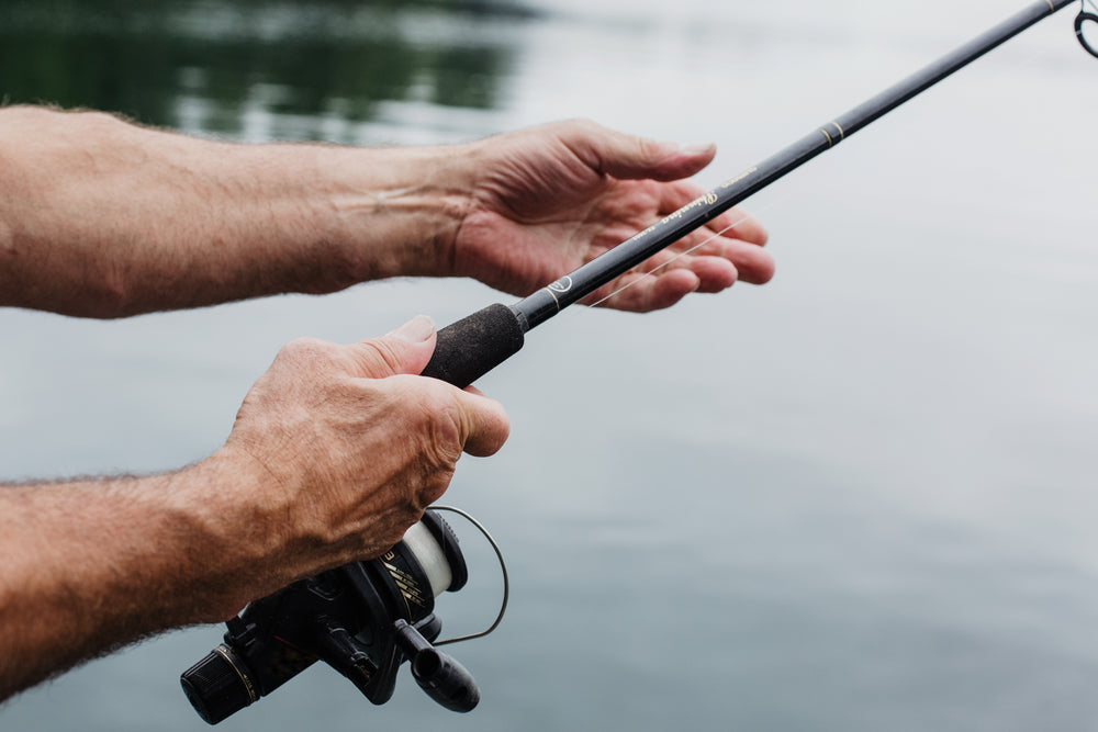 aged hands hold a fishing rod over still waters