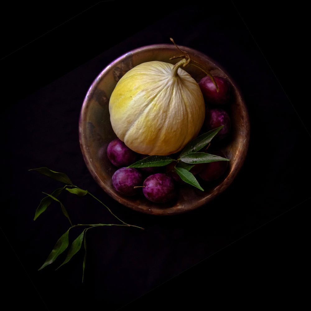 an aged melon in a bowl of plums