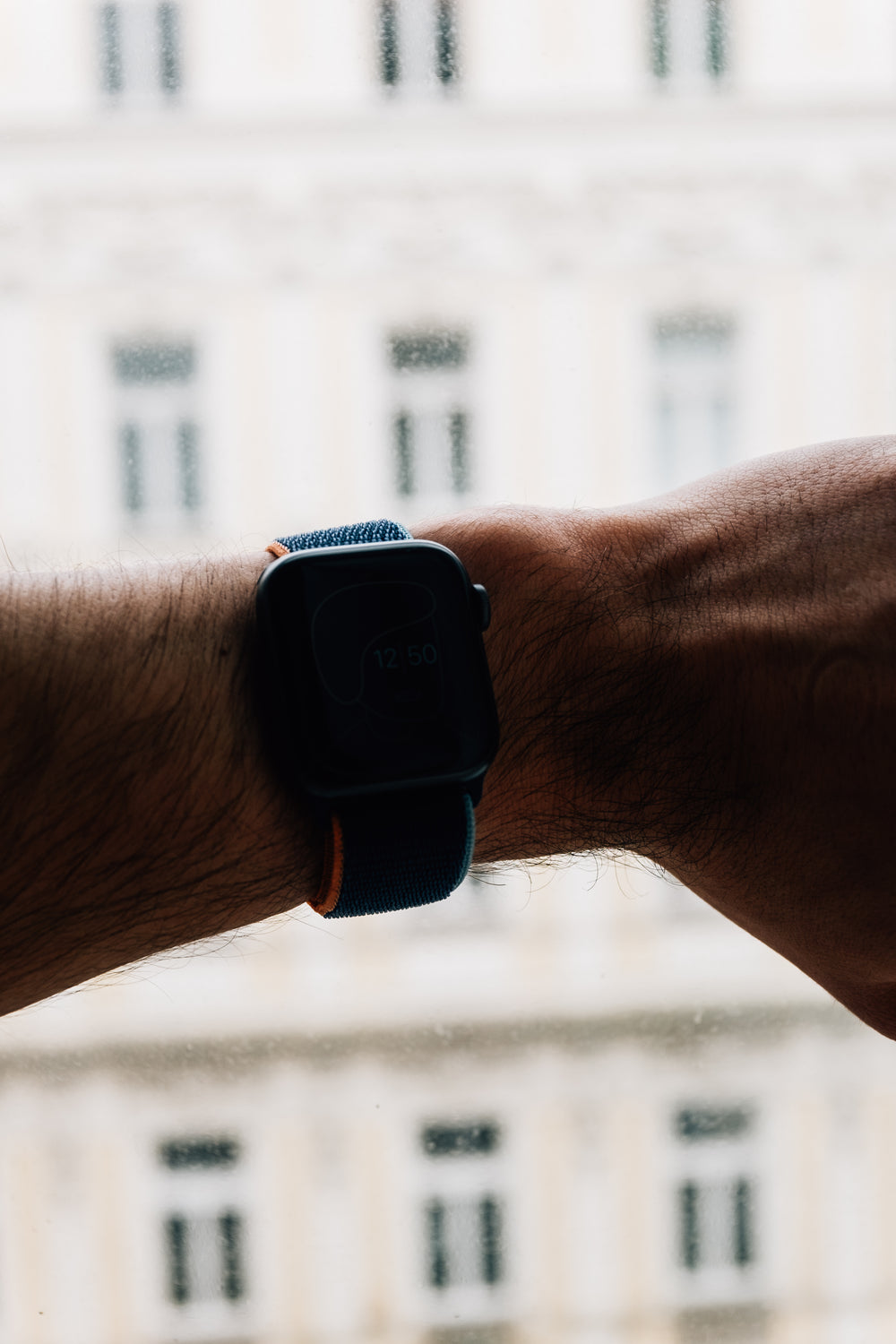 an arm wearing a smartwatch is backlit by window light