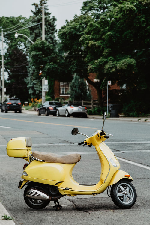 an italian summery yellow moped parked on a street
