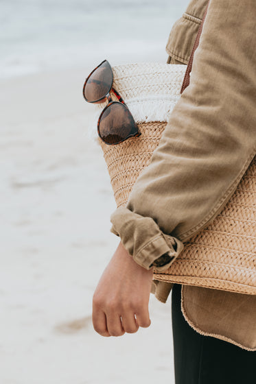 arm resting on a wicker beach bag with sunglasses on it