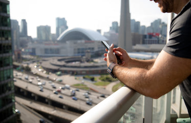 arms lean on a balcony railing holding their phone