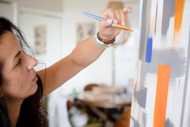 artist holds a paint brush up to there canvas