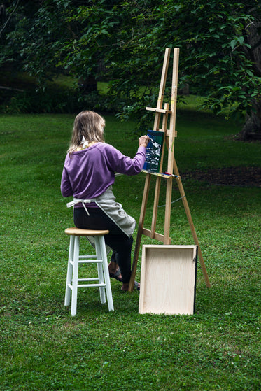 artist sits outdoors and paints at an easel
