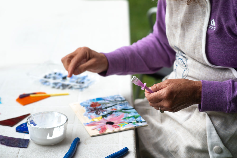 artist works on a floral mosaic with white glue