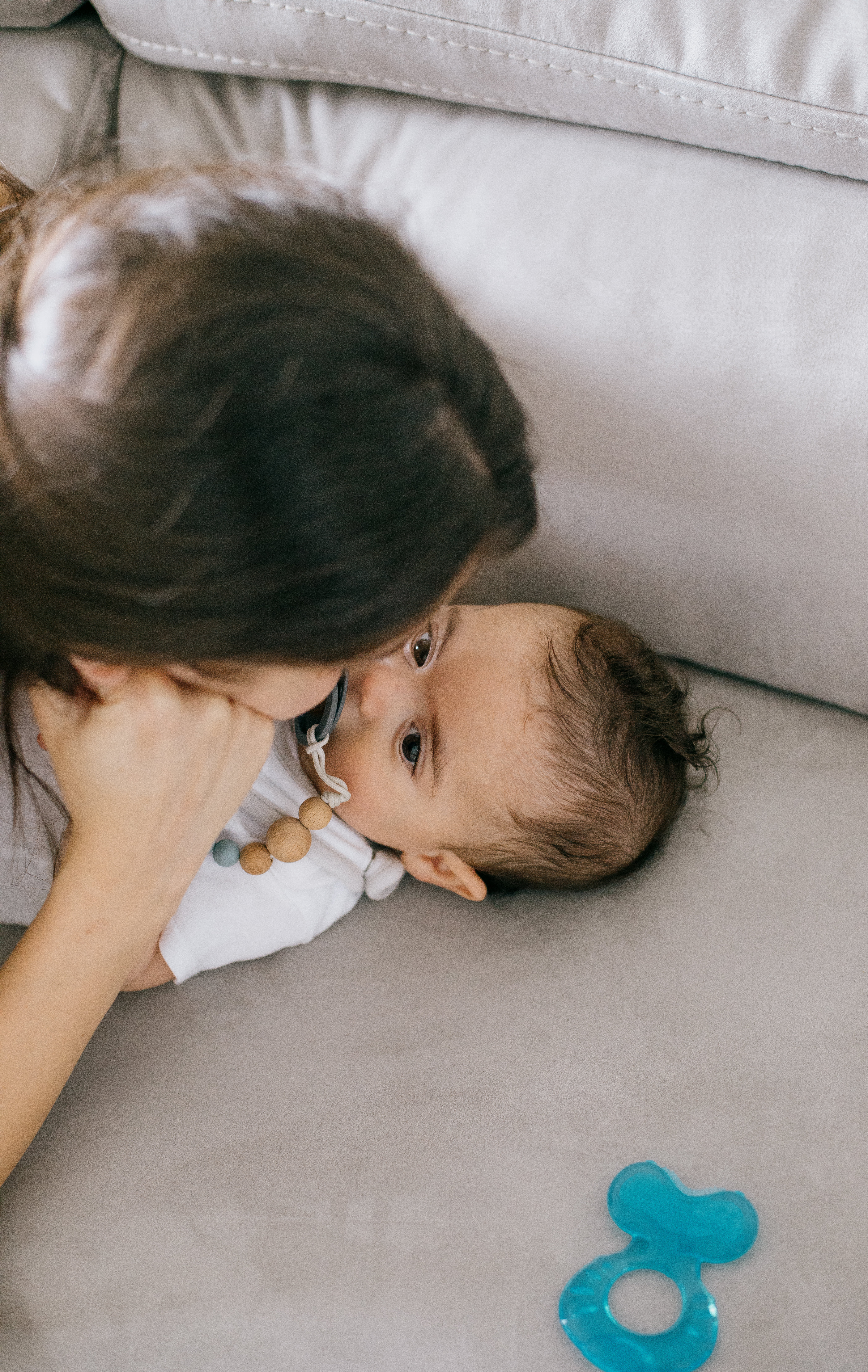 Baby And A Person Lay Close On A White Couch