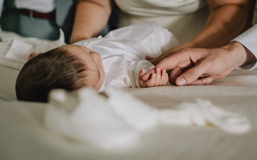 baby lays down and holds a adults finger