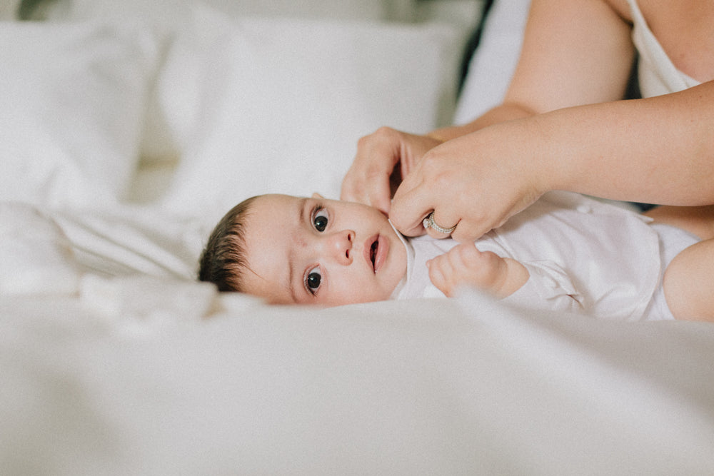 baby lays on white duvet looking at the camera