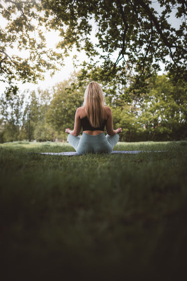 back of a woman sitting outdoors on a mat