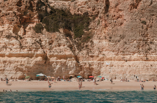 bathers bask on a sunny beach under rocky cliffs