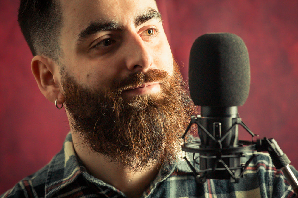 bearded man standing behind a black microphone