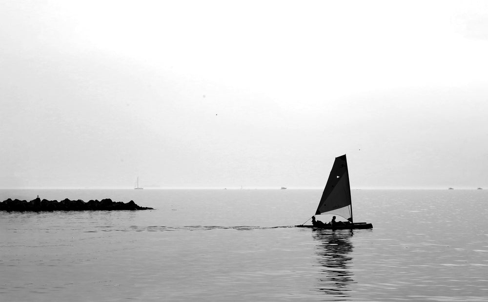 black and white photo of a sail boat on still water