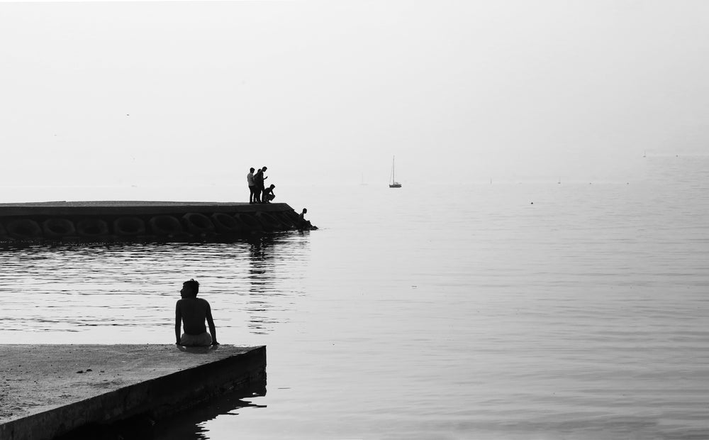 black and white photo of people on a cement shore by still water