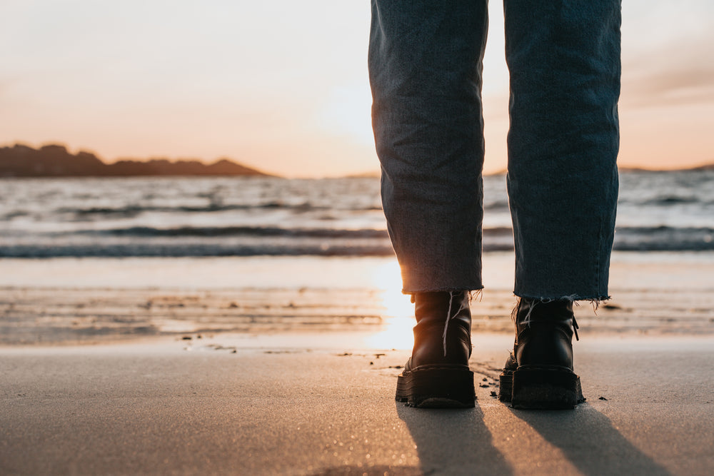 black boots and legs on a sandy beach at sunset