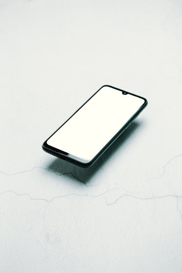 black cellphone floats over a white surface
