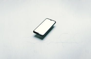 black cellphone with lit screen floating over white background