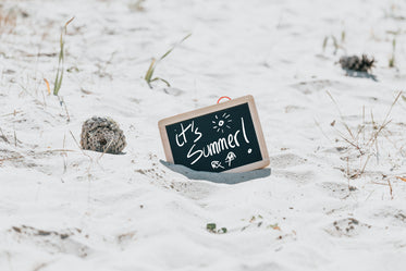 black chalkboard in the sand reads its summer