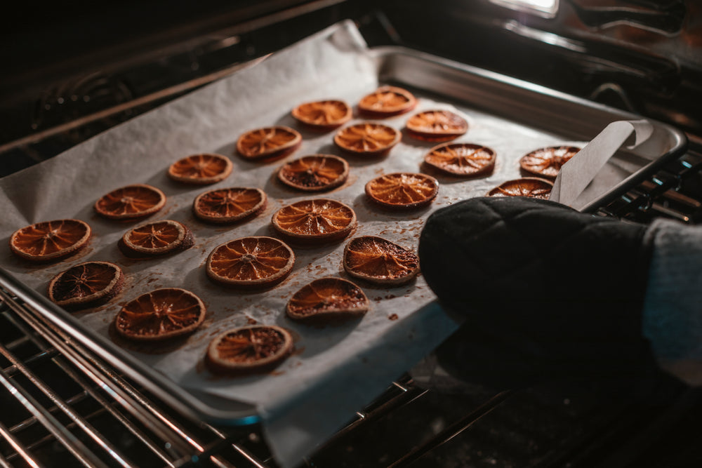 black oven mitt holds tray of oranges in the oven
