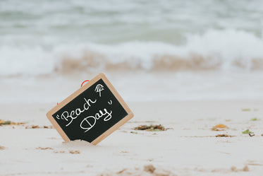 blackboard that reads beach day sticks out of a sandy beach