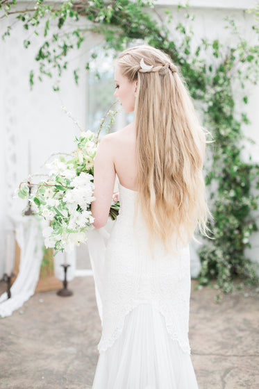 blond person in a white dress holds a large bouquet of flowers