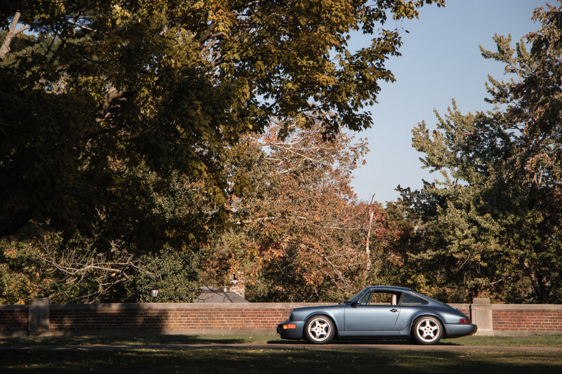 blue car parked by small brick wall surrounded by trees