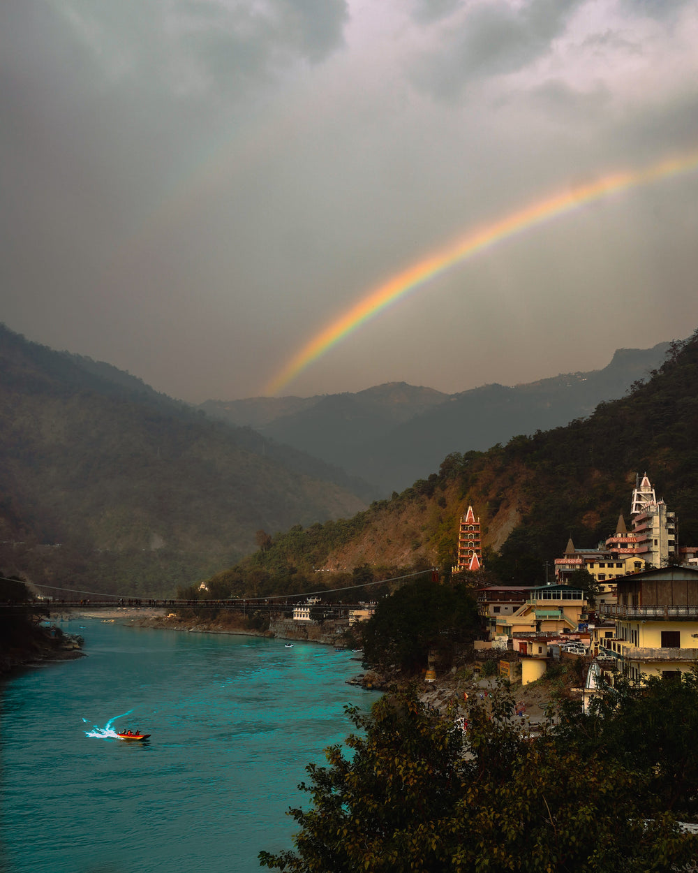 blue river between two hills with a vivid rainbow arching above