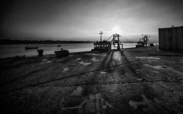 boats docked against a cement shore in black and white