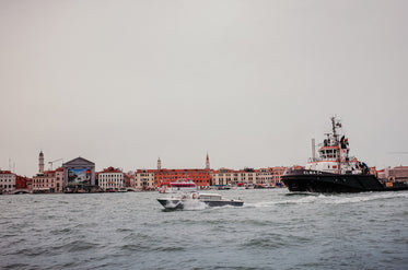 boats on wavy water with the shore lined with buildings