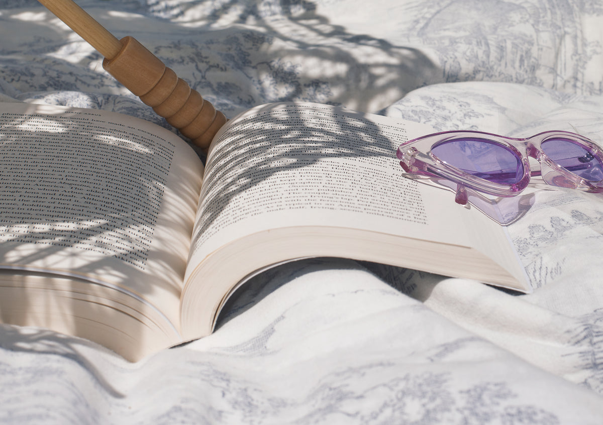 book lays open next to purple cateye sunglasses