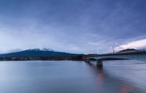 bridge over still water reaches to a large snowy mountain