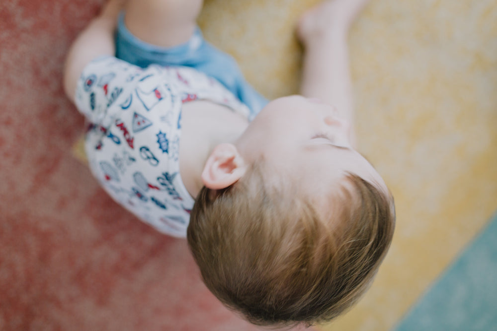 camera looks down at a small child on colorful rug