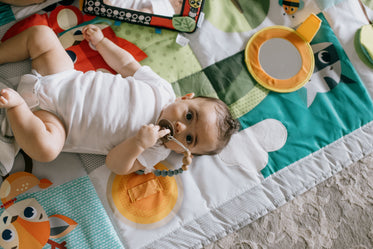 camera looks down to a baby laying in a colorful mat