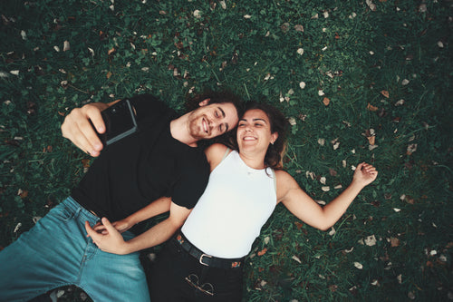 camera looks down towards a couple laying on green grass