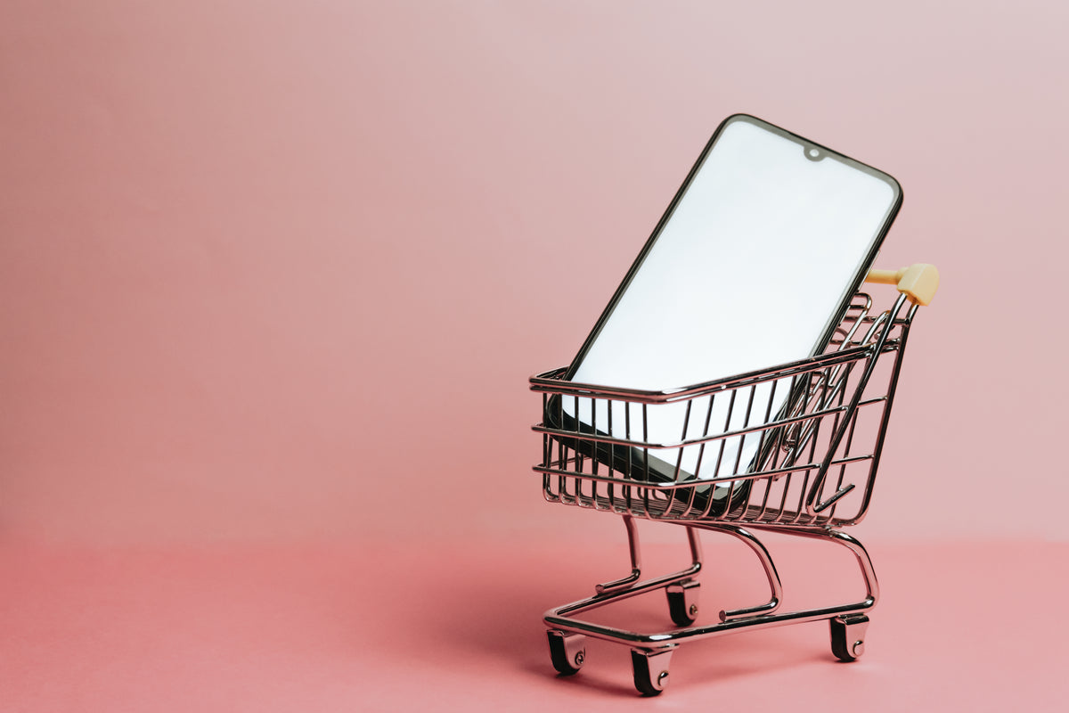 cell phone sits in a small shopping cart against pink