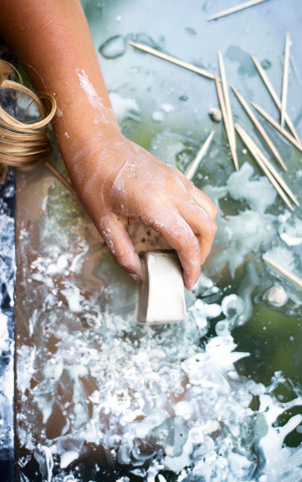 childs hand holds a block of pottery clay