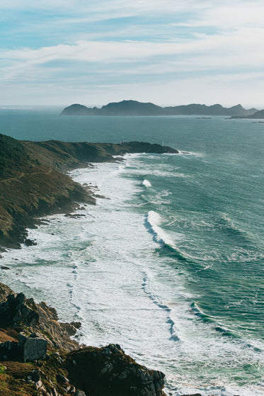 cliff side view of wavy ocean and large hills