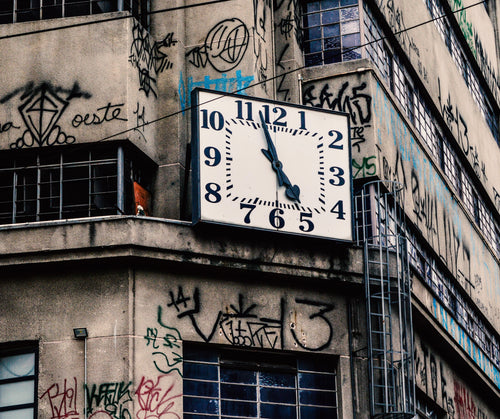 clock on on a building with black graffiti