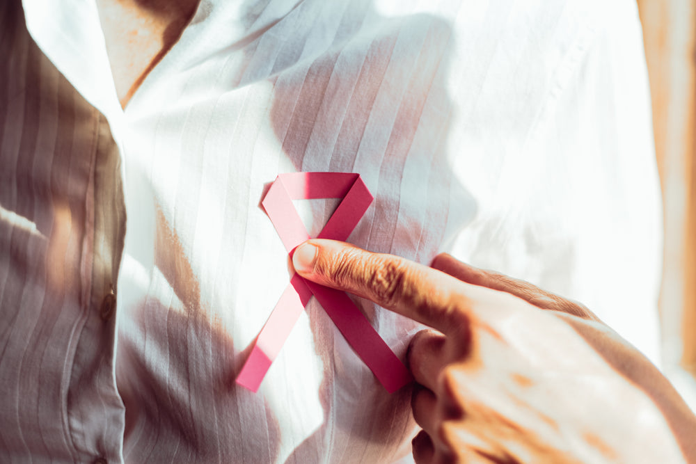 close up of a person holding a pink ribbon on their chest