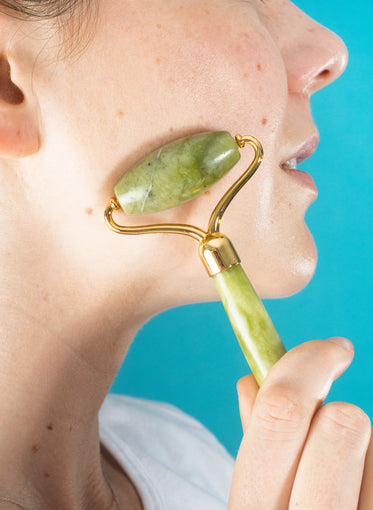 close up of a person using a jade roller on their cheek