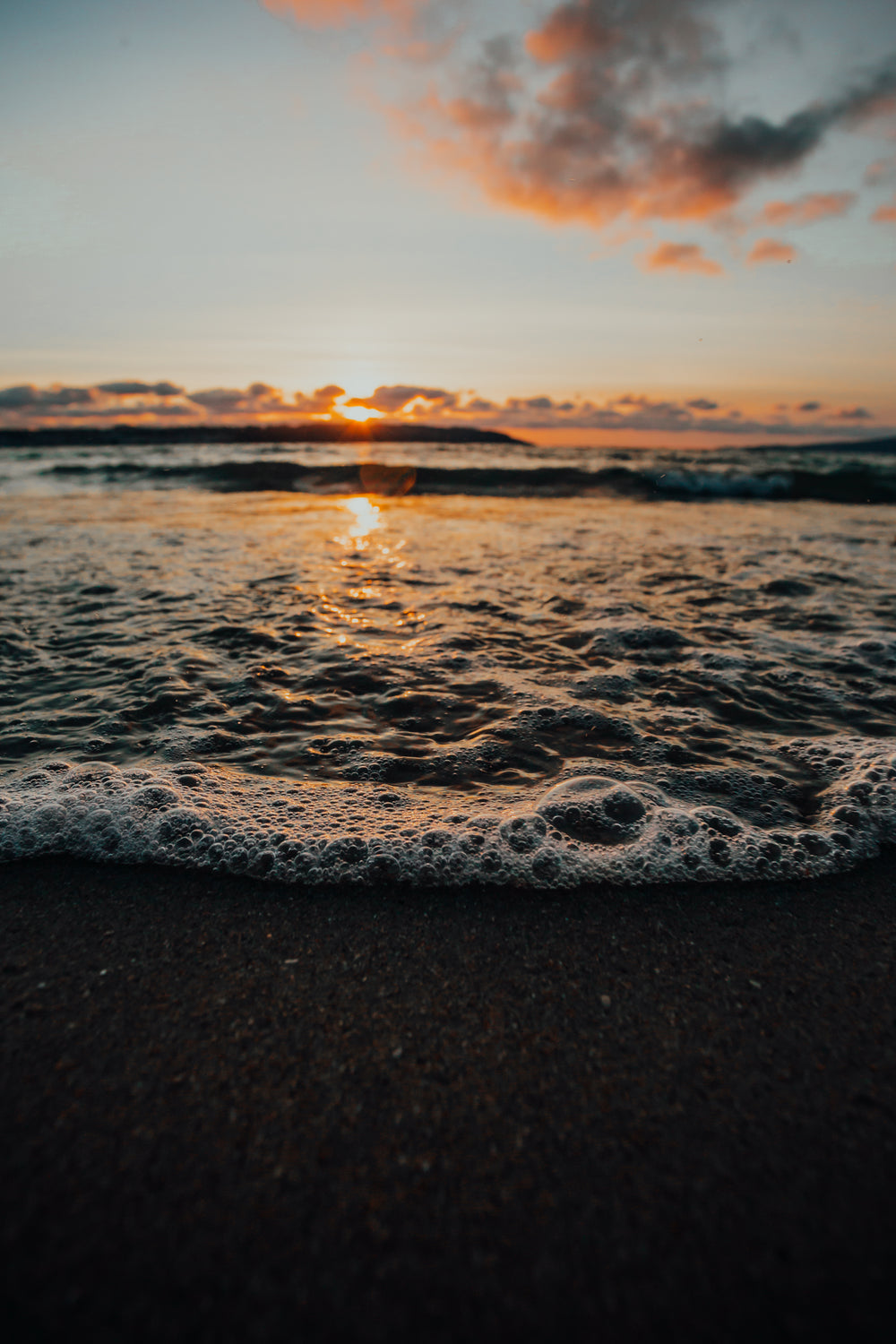 close up of waves and bubbles on the shore at sunset