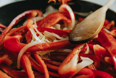 close up of white onions and red peppers cooking in a pan